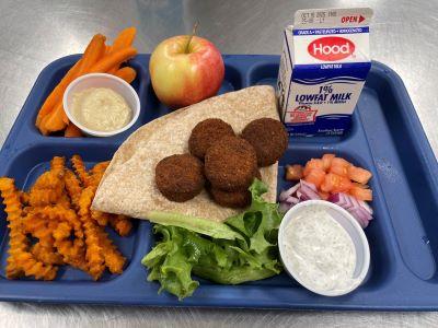 School meal tray with falafel, wheat wrap, sweet potato fries, carrot sticks and dip, apple, milk,